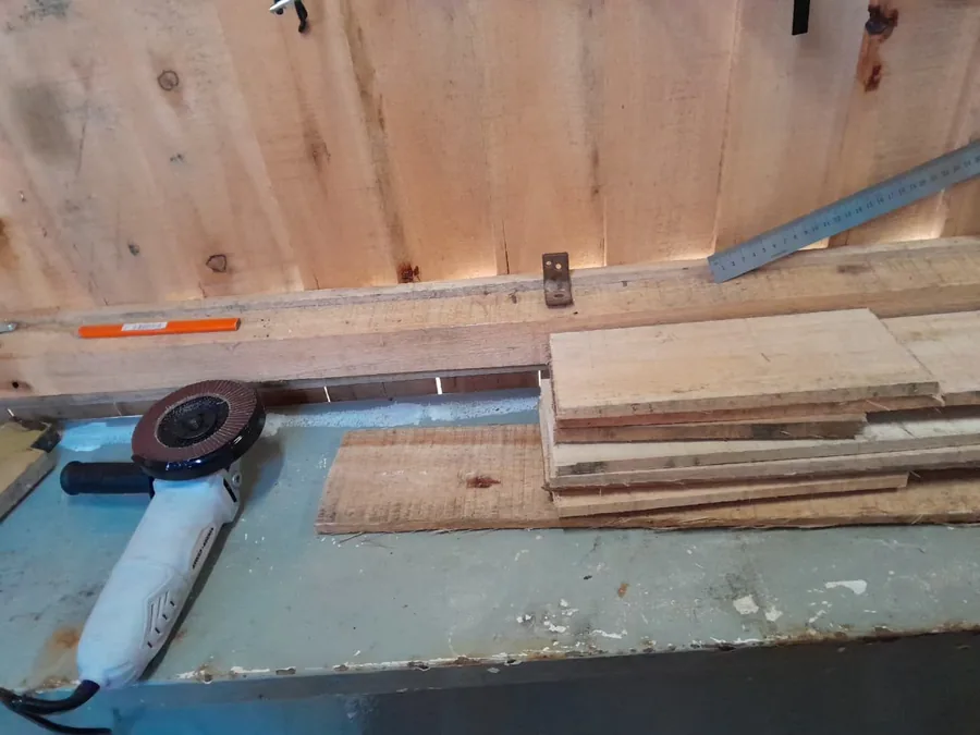 Mesa de trabajo del taller con tablas apiladas, una amoladora y las herramientas colgadas de la pared