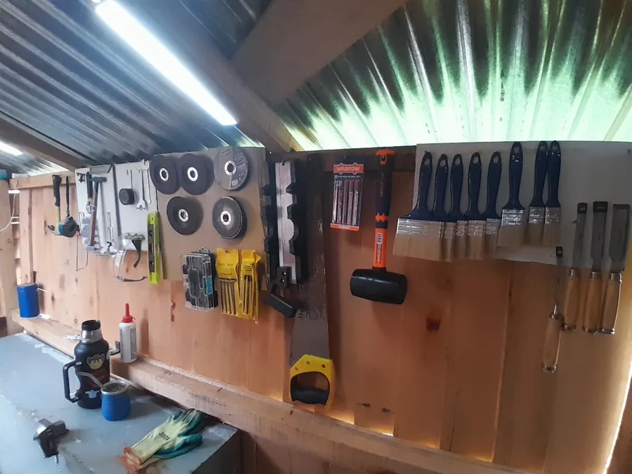 Pared del taller con pinceles, martillo de goma, serrucho, formones y discos de corte colgados